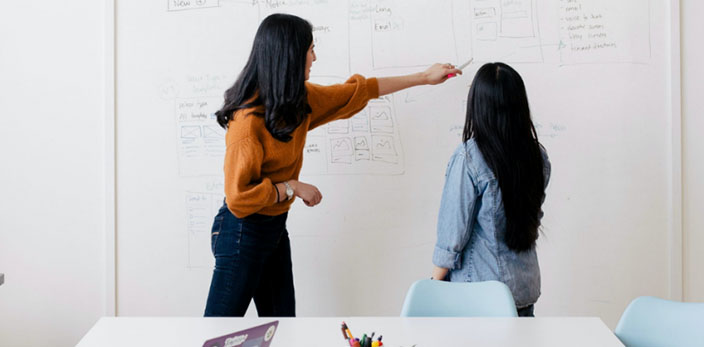 woman pointing on something on a white board to another woman