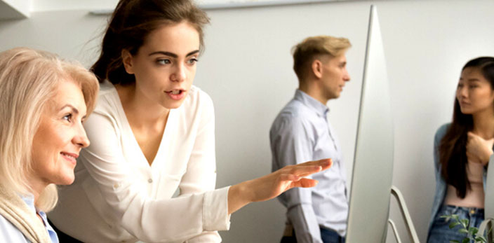 younger woman professional helping older woman professional about work