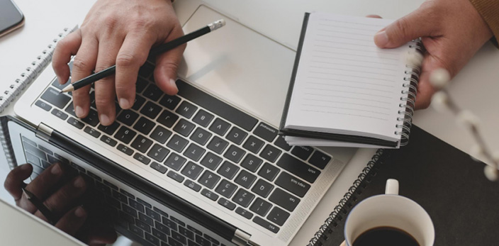 Close up of person taking notes on notebook while on laptop