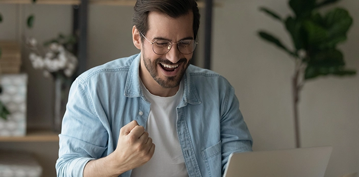 creating-positive-candidate-experience-happy-man-with-glasses-raising-fist-feeling-fulfilled-laptop